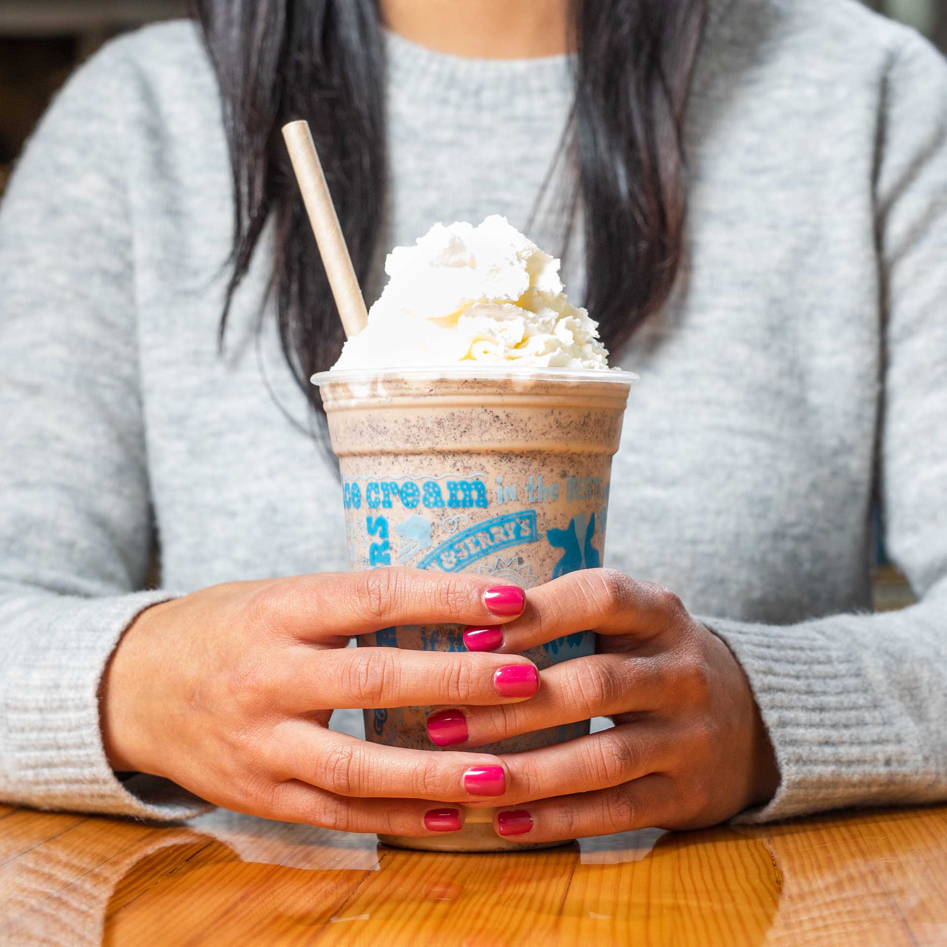 Person seated at a table holding an ice cream shake