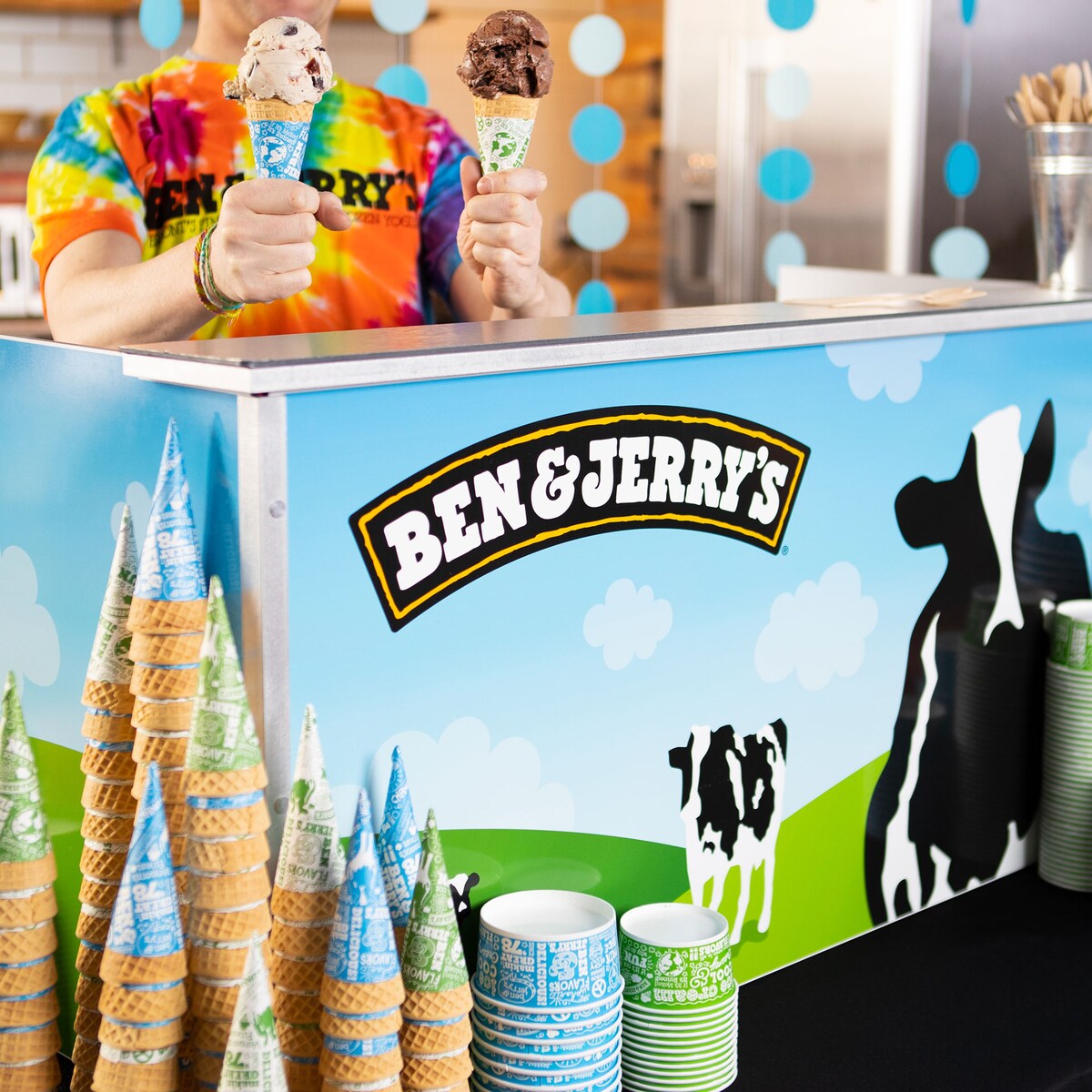 A person holding two ice cream cones behind a counter